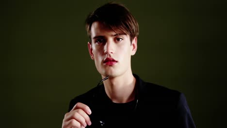 androgynous man posing with sunglasses against green background