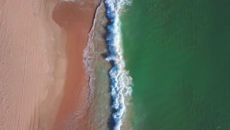 aerial tilt down shot to waves reaching a sandy beach in the south of spain