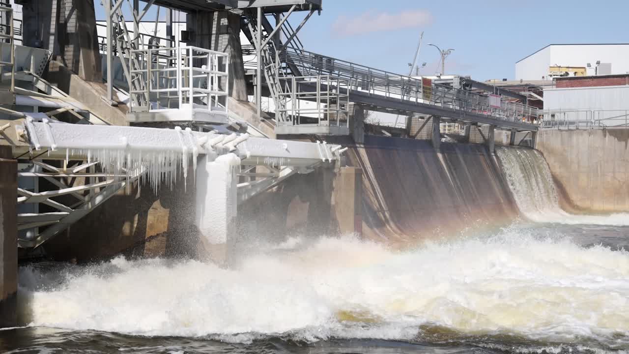 River flowing through dam with some ice on dam wide shot.