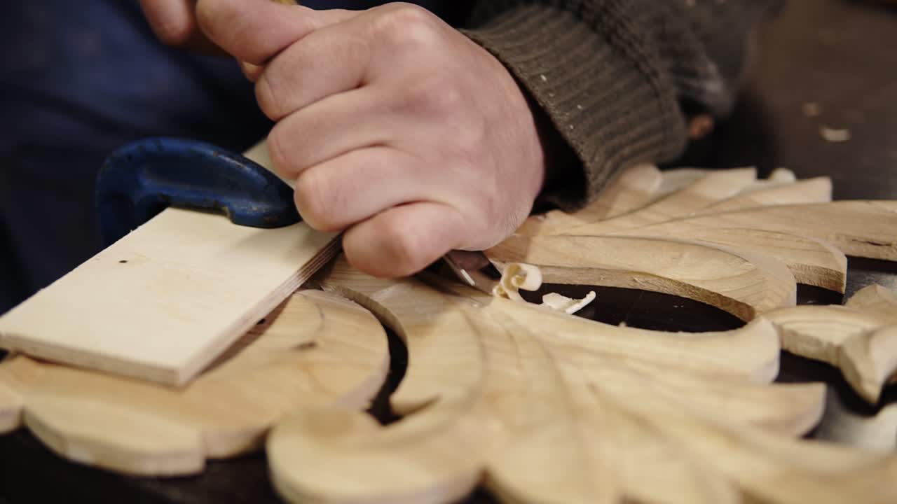 Carpenter working on a wooden in his workshop on the table, preparing a detail of wooden product, a part of future furniture. Close up footage of a man's hands cuts out patterns with a planer