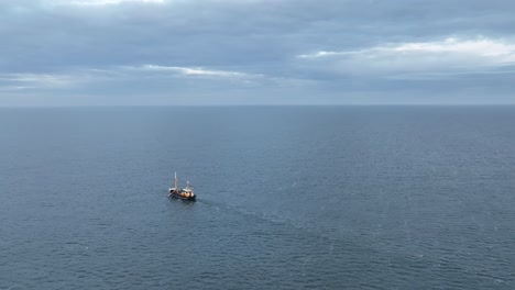 Panning-drone-shot-of-a-Fishers-boat-dragging-the-nets-thru-the-water-of-the-shore-of-Ameland