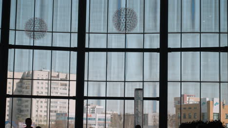 a modern building interior featuring large floor-to-ceiling windows with cityscape views. silhouettes of people and indoor plants are visible in the foreground