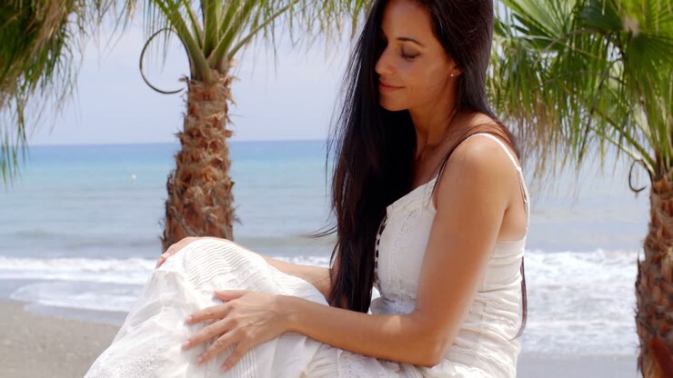 frau in weißem kleid sitzt an der strandwand