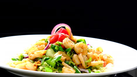 a well arrange shrimp salad on a white plate with a black background