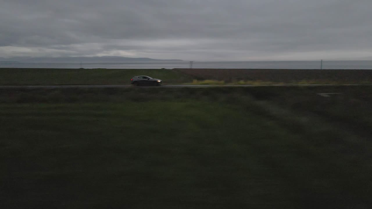 차 가 황혼 에 외 ⁇  도로 를 가로지르고, 그 헤드라이트 가 황혼 을 가로지르고 멀리 있는 산 들 의 멋진 실루 ⁇  이 지평선 에 나타나고 있다