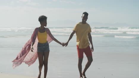 African-american-couple-holding-hands-smiling-while-walking-on-the-beach