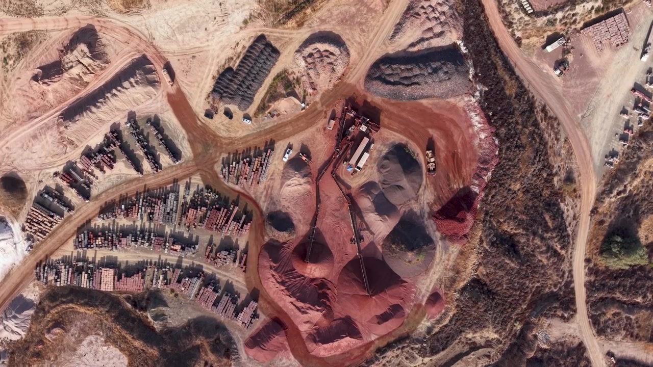 Aerial view of clay mining site with machinery, stockpiles, and rugged terrain