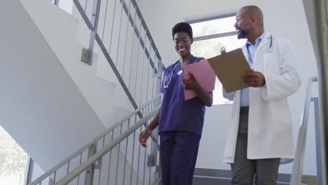 African-american-male-and-female-doctors-holding-clipboard-and-talking-at-hospital