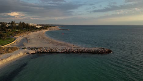 aerial flyover sandy beach with walking and relaxing people during golden sunset at south beach in fremantle, western australia