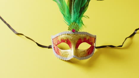 video de una máscara de carnaval dorada y roja con plumas verdes sobre un fondo amarillo.