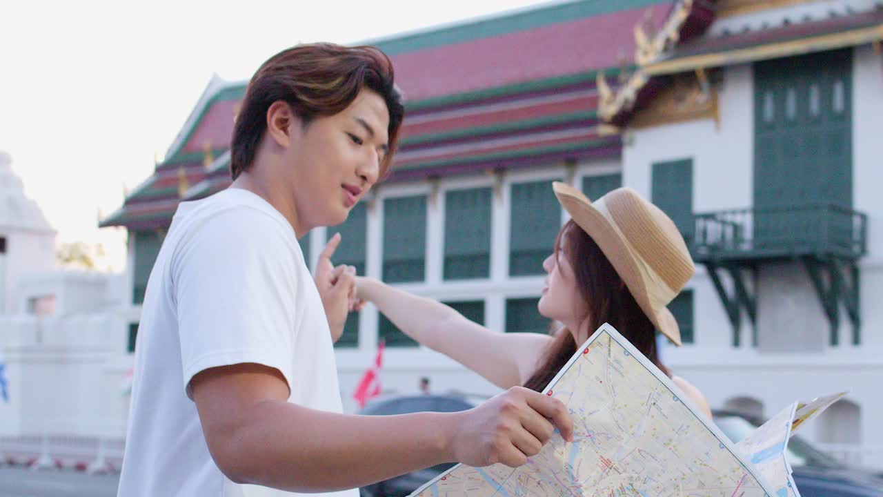 Smiling tourist couple studies paper map near ornate temple at sunset, handheld medium shot