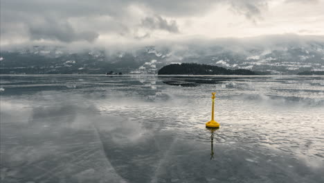 yellow special mark buoy on frozen steinsfjorden lake with clouds in norway