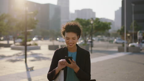 Retrato-De-Una-Joven-Mujer-De-Negocios-Hispana-En-Prácticas-Sonriendo-Disfrutando-De-La-Navegación-De-Mensajes-De-Texto-Usando-La-Aplicación-De-Redes-Sociales-Para-Teléfonos-Inteligentes-En-La-Ciudad-Al-Atardecer