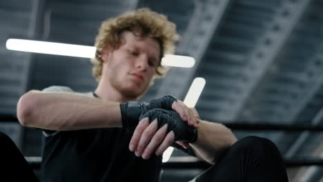 Agitated-fighter-preparing-to-wear-gloves-at-gym