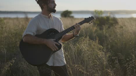 man playing acoustic guitar in a field at sunset