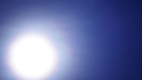 the sun or moon passes diagonally through the frame behind a thin veil of clouds in time-lapse motion