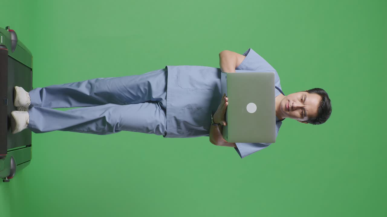 cuerpo lleno de médico masculino asiático con estetoscopio usando una computadora portátil mientras camina en el fondo de la pantalla verde en el hospital