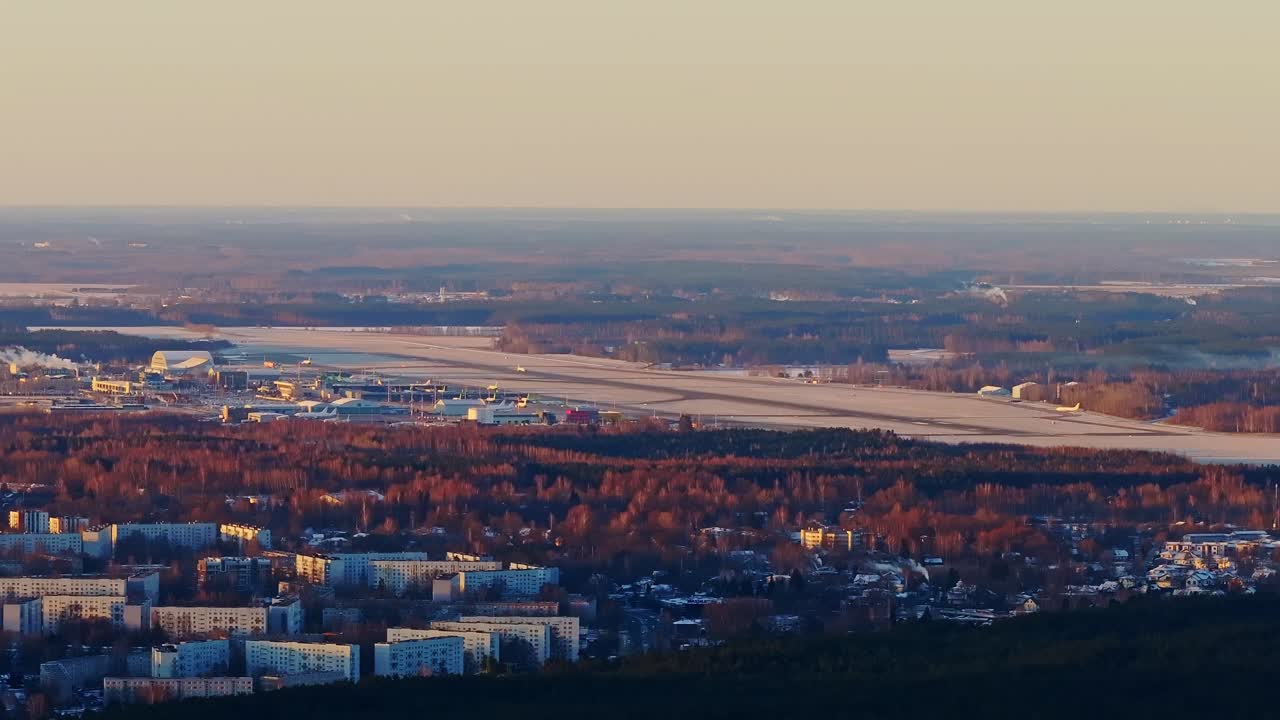 Plane takes off at dawn over Riga Airport, seen from afar glowing spring sunrise