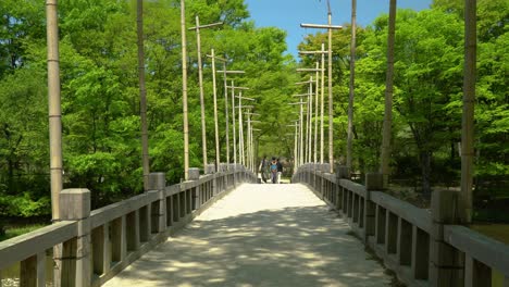 friends walking at an old wooden bridge with lush green trees at korean folk village in yongin, seoul, south korea