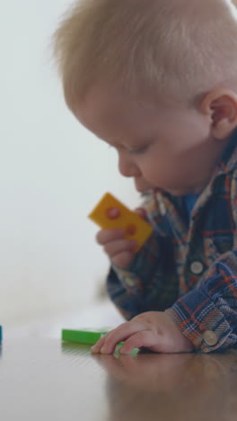 cute little baby plays with color plastic toy standing at low wooden table in light children room close view