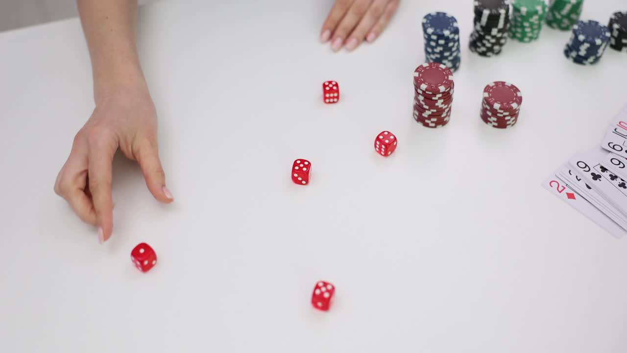 A person's hands interacting with dice, poker chips, and playing cards on a white table