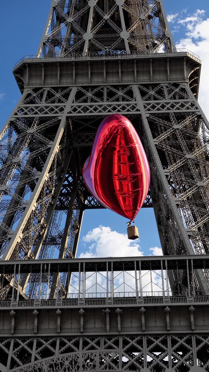 A low-angle video captures a red heart-shaped balloon floating in front of the Eiffel Tower