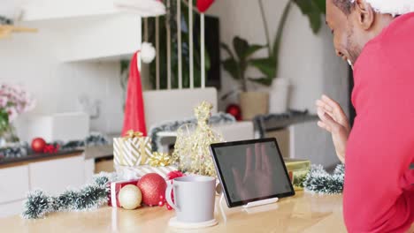 Happy-african-american-man-wearing-santa-hat,-using-tablet-with-copyspace