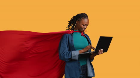 Young-girl-wearing-superhero-for-Halloween-working-on-laptop,-studio-background