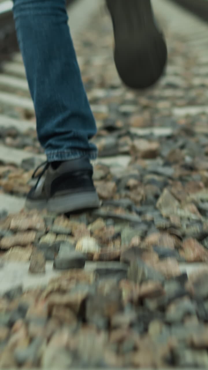 A close view of someone running on a railway track, wearing jeans and canvas shoes, the track is covered with stones
