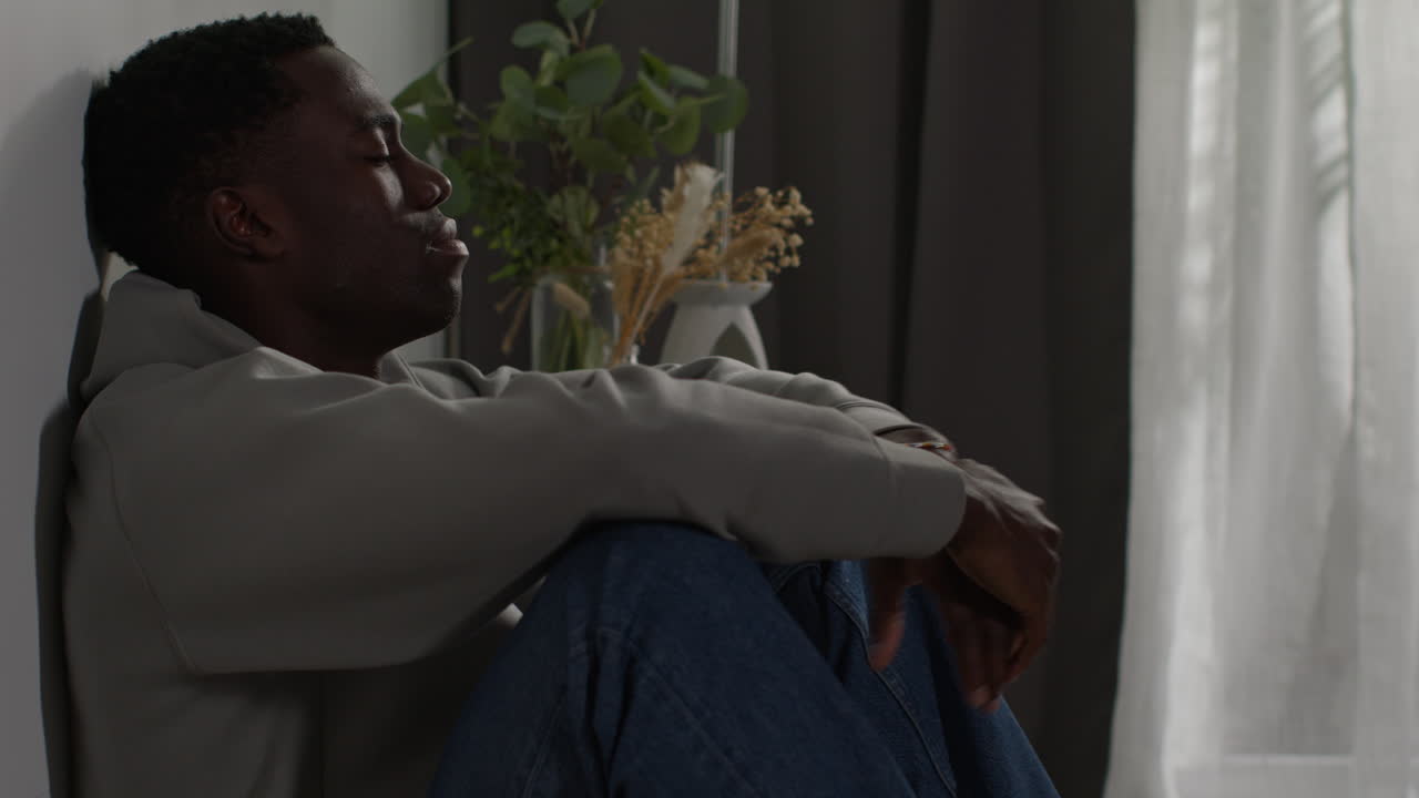 Young Man With Mental Health Issues Sitting On Floor At Home By Window Shaking Head Looking Depressed And Unhappy 1