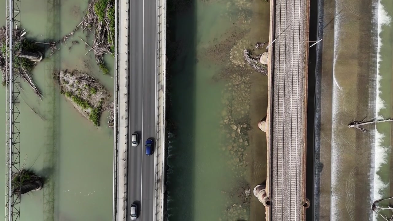 Ponti stradali e ferroviari che attraversano il fiume Trebbia vicino a Piacenza, Emilia-Romagna, Italia, mostrando i canali del fiume, le infrastrutture idrauliche e i corridoi di trasporto all'interno della Pianura Padana, con una vista dall'alto.