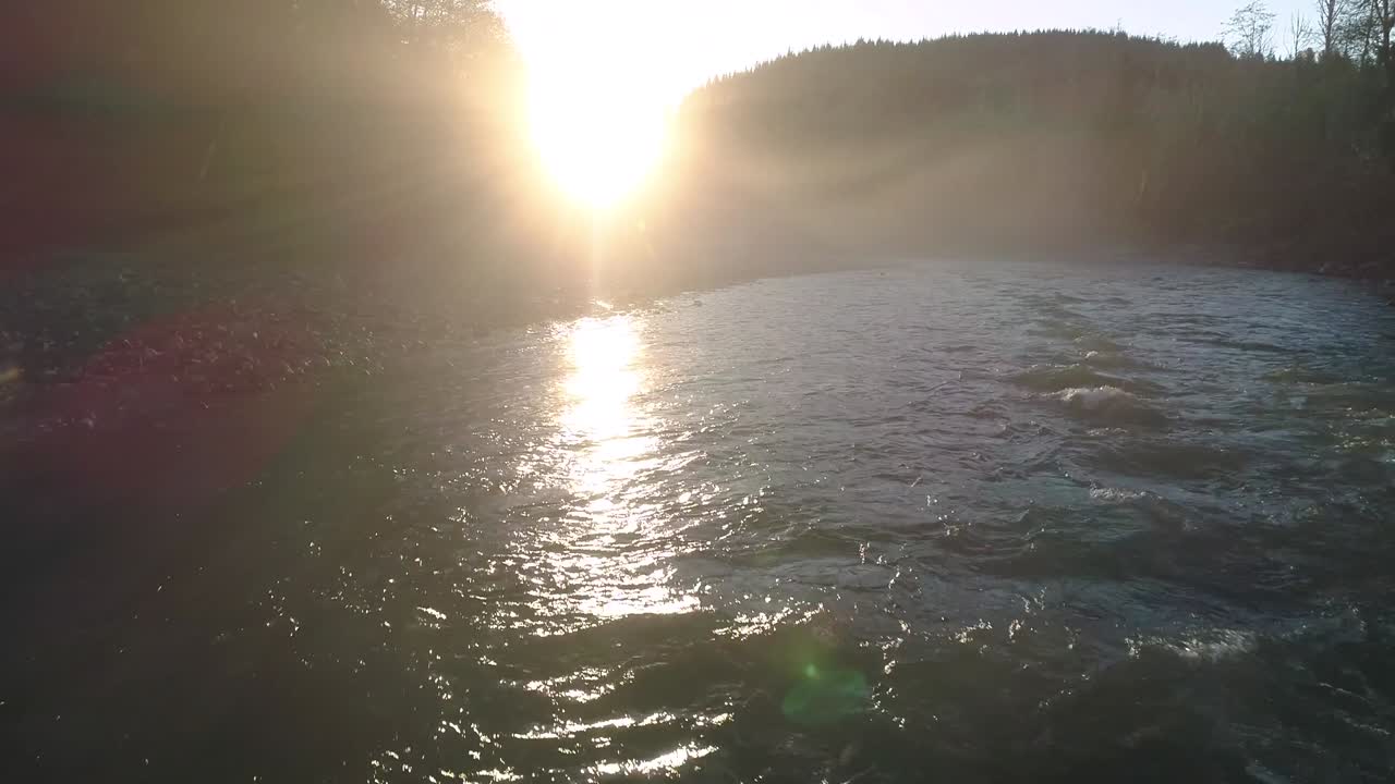 низкий полет беспилотника над рекой, быстрые волны в туманном закате.