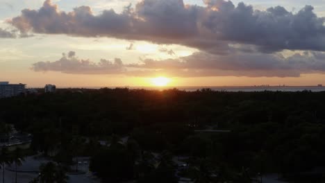 dolly en el ascenso de una toma aérea de un impresionante atardecer amarillo dorado del océano con vegetación tropical debajo de crandon park en key biscayne fuera de miami, florida en una cálida y soleada noche de verano