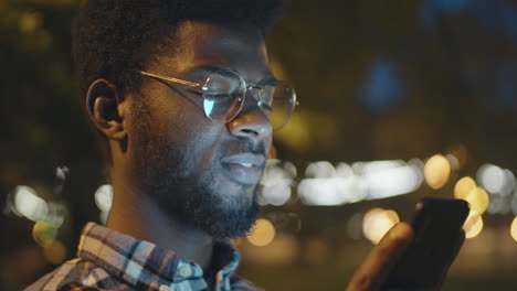 cheerful black man using smartphone outdoors in evening