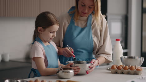 Alegre-Madre-E-Hija-Están-Cocinando-En-La-Cocina-De-Casa-La-Mujer-Está-Enseñando-A-La-Niña-A-Cocinar-Pastel