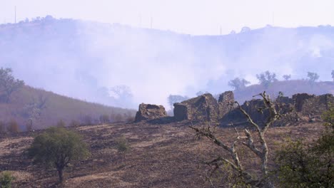 el humo todavía cuelga sobre las ruinas de una casa de montaña después de un incendio forestal
