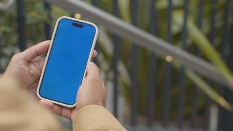 close up of muslim man sitting outdoors on city street looking at blue screen mobile phone 2