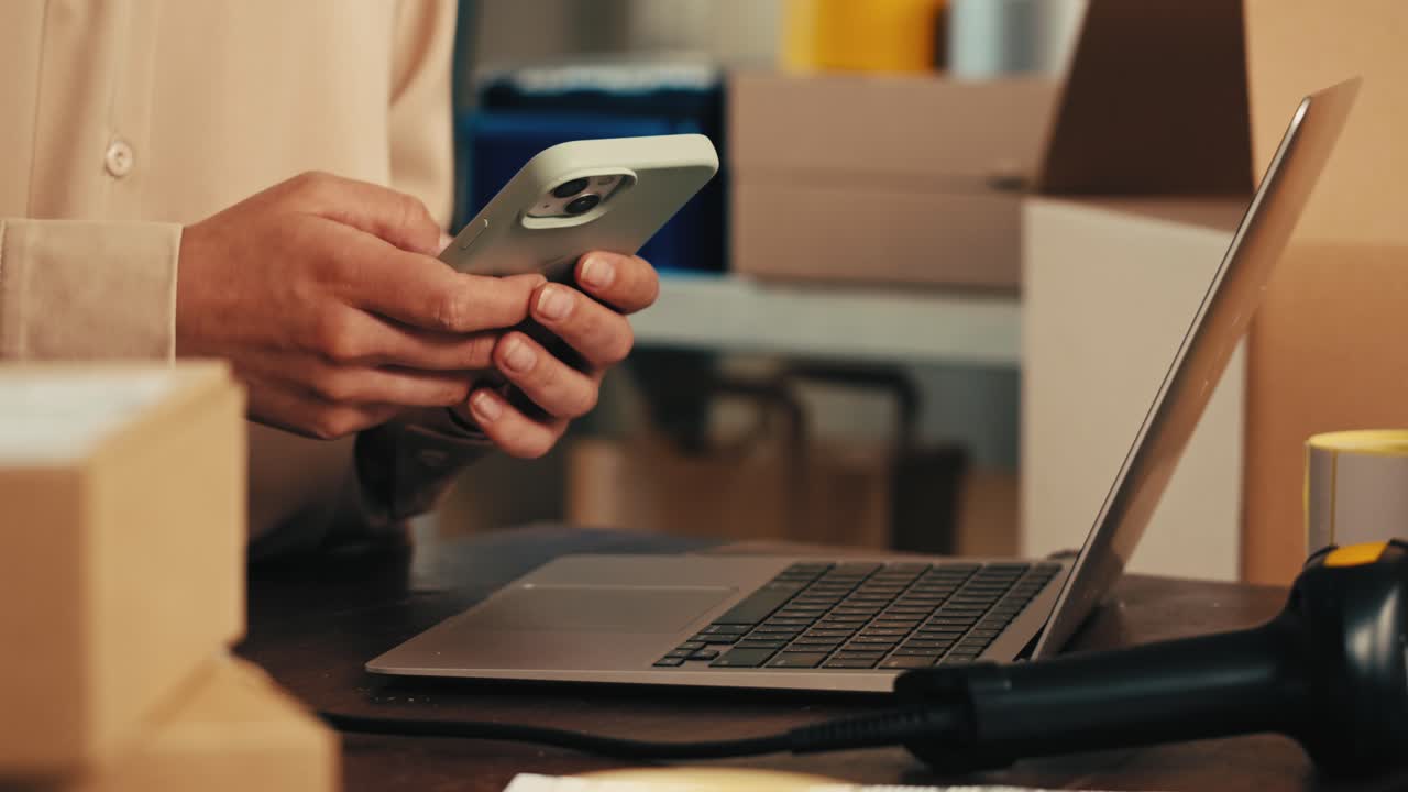 Person using smartphone and laptop in a warehouse or office