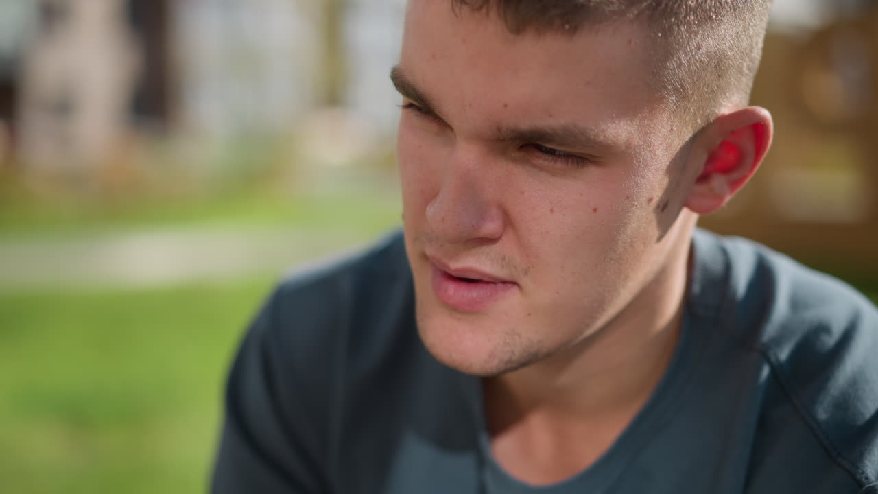 close up of boy tilting head slightly while seated outdoors under warm sunlight showing calm expression with green blur background suggesting relaxation self-reflection
