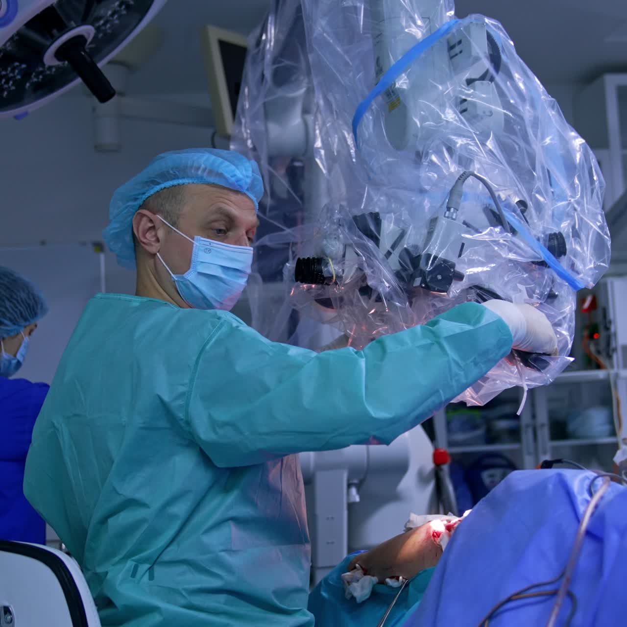 Surgeons gives the instrument to a nurse. Doctor pulls closer the microscope covered in plastic and adjusts it to his eyes and incision on a patient's body