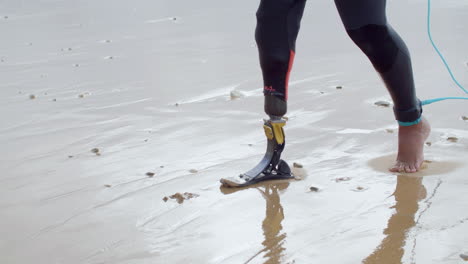 close up of an unrecognizable man in wetsuit with bionic leg walking along the seashore