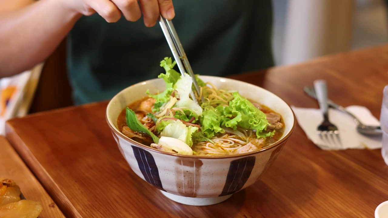 Primo piano di una persona che usa bacchette di metallo per mangiare la zuppa di noodle vietnamita bun cha.