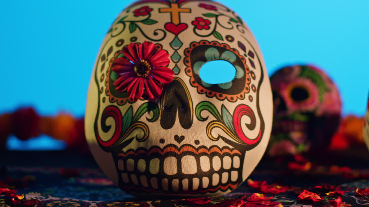 close up de cráneos decorados y máscaras rodeadas de pétalos de flores celebrando la fiesta mexicana de dia de muertos o día de los muertos contra fondo azul 4