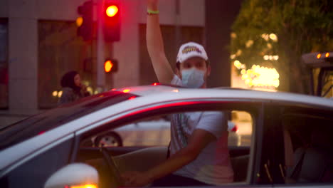 a man holds up his fist through the sunroof of his car in support of blm protesters in the streets of downtown.