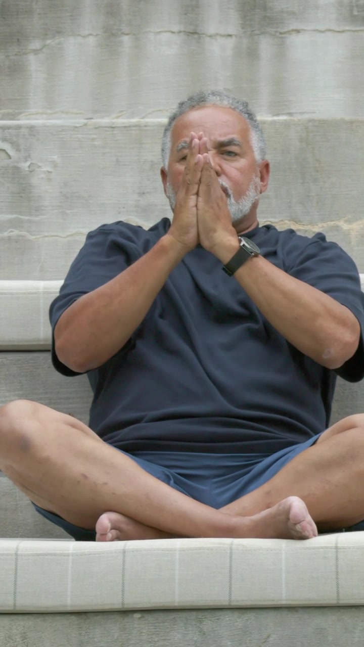 Video verticale: Uomo con maglietta blu scuro e pantaloncini che entra nell'inquadratura, solleva i palmi e respira sui gradini, con orologio smart.