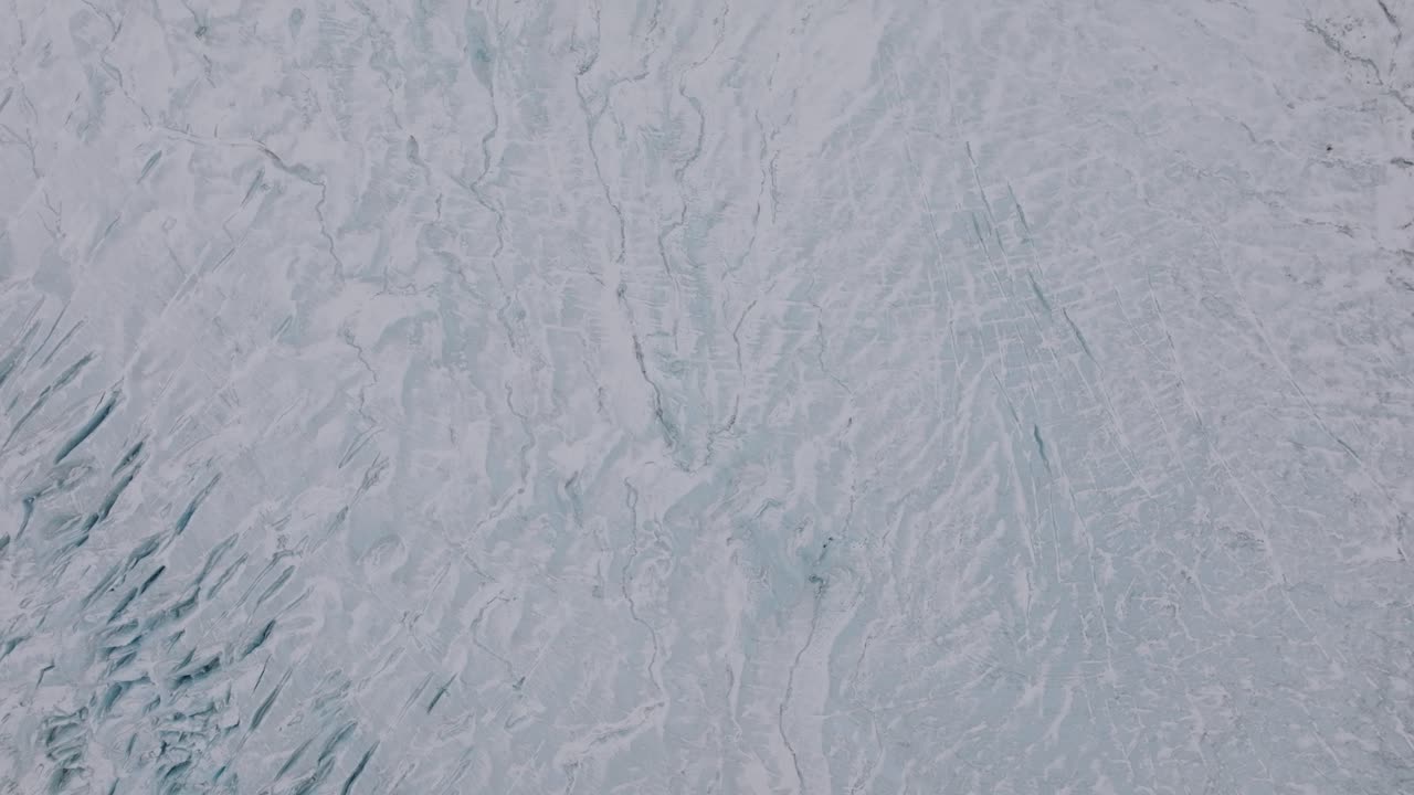 Aerial top view over ice cracks and formations in Virkisjokull glacier covered in snow, Iceland