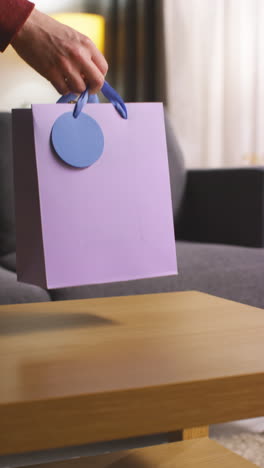 vertical video of person putting present in gift bag with tag on table in lounge