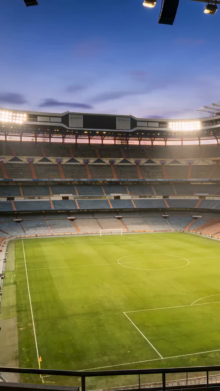 Vertikales Video: Wandernde Sonne lässt leeres Stadionfeld leuchten, während Flutlichter bei Sonnenuntergang angehen.