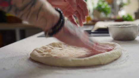 hands flattening dough for pizza