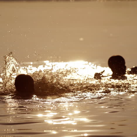 Kids having fun in water outdoors. Silhouette of happy little boys playing in river water in the evening. Summer fun.